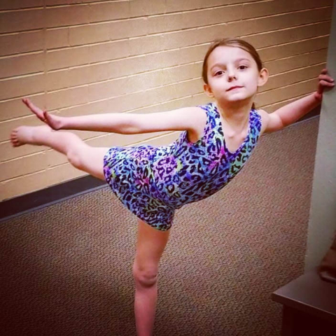 Young girl modeling metallic print leopard print gymnastics leotard with attached skirt.