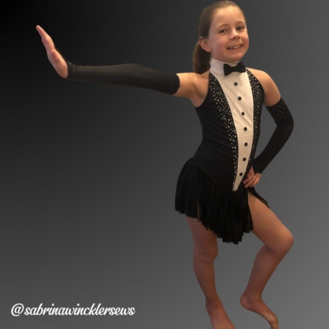 Girl wearing a tuxedo themed figure skating dress with fringe skirt and fingerless gloves